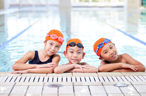 Three children at the end of a pool wearing swim caps and goggles-an image of a childhood hobby