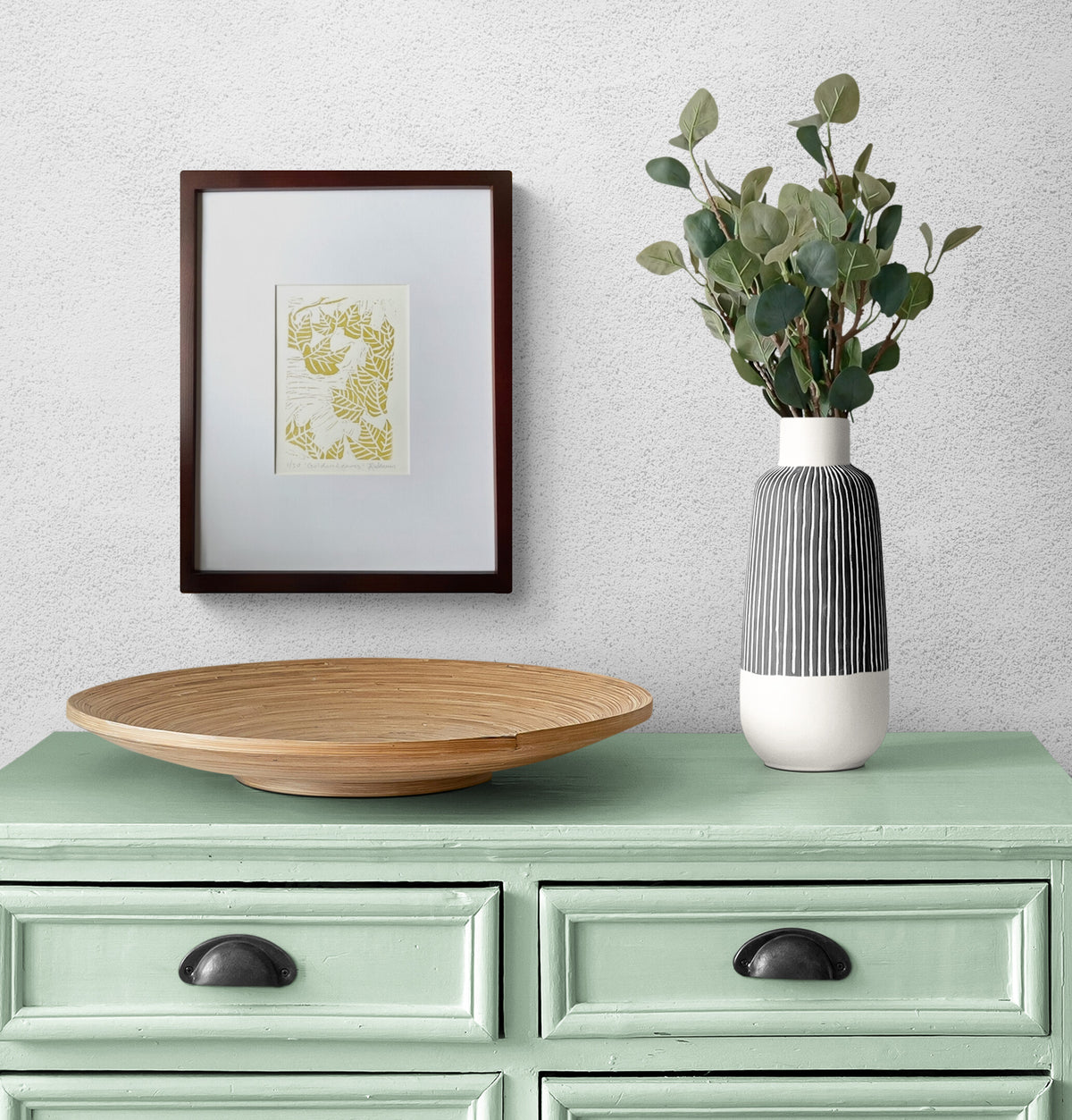 Fall leaf linocut print by Katie Weaver in gold ink displayed above a dining room hutch with simple decor