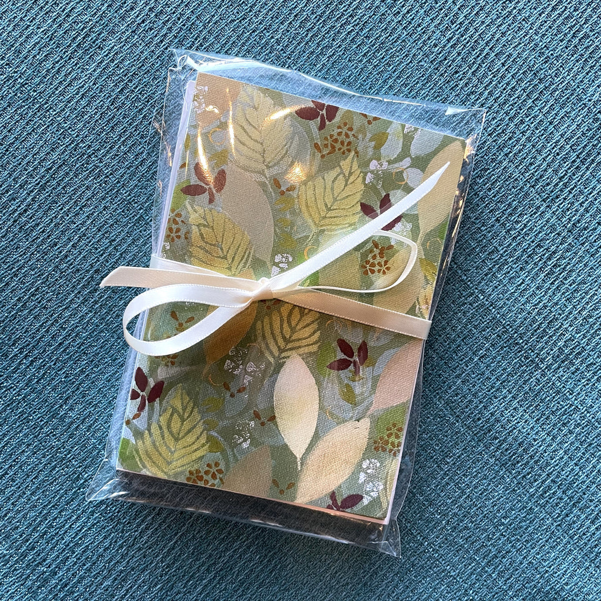 Package of holiday leaf notecards tied with a ribbon featuring warm autumn leaf artwork by Katie Weaver