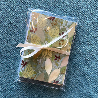 Package of holiday leaf notecards tied with a ribbon featuring warm autumn leaf artwork by Katie Weaver