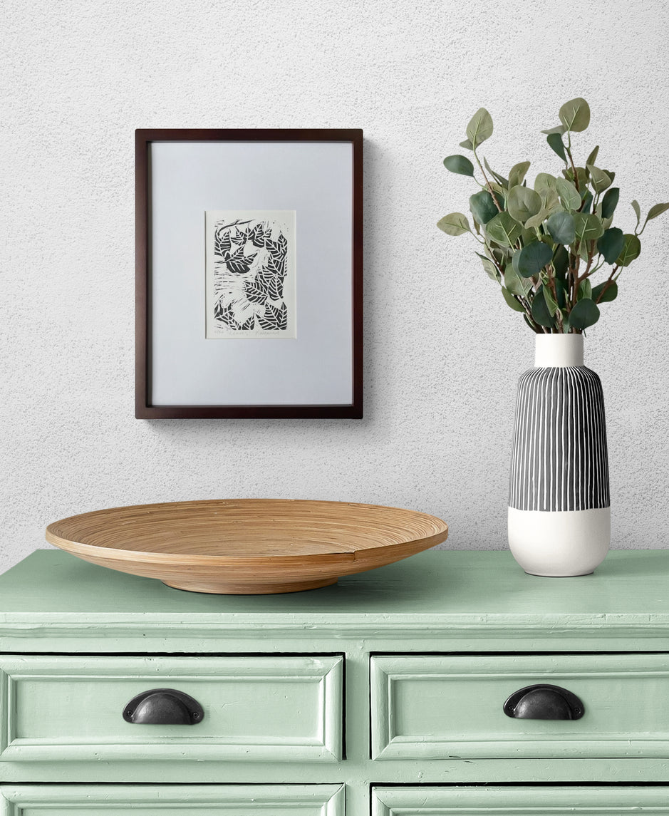 Fall leaf linocut print by Katie Weaver in black ink displayed above a dining room hutch with simple decor