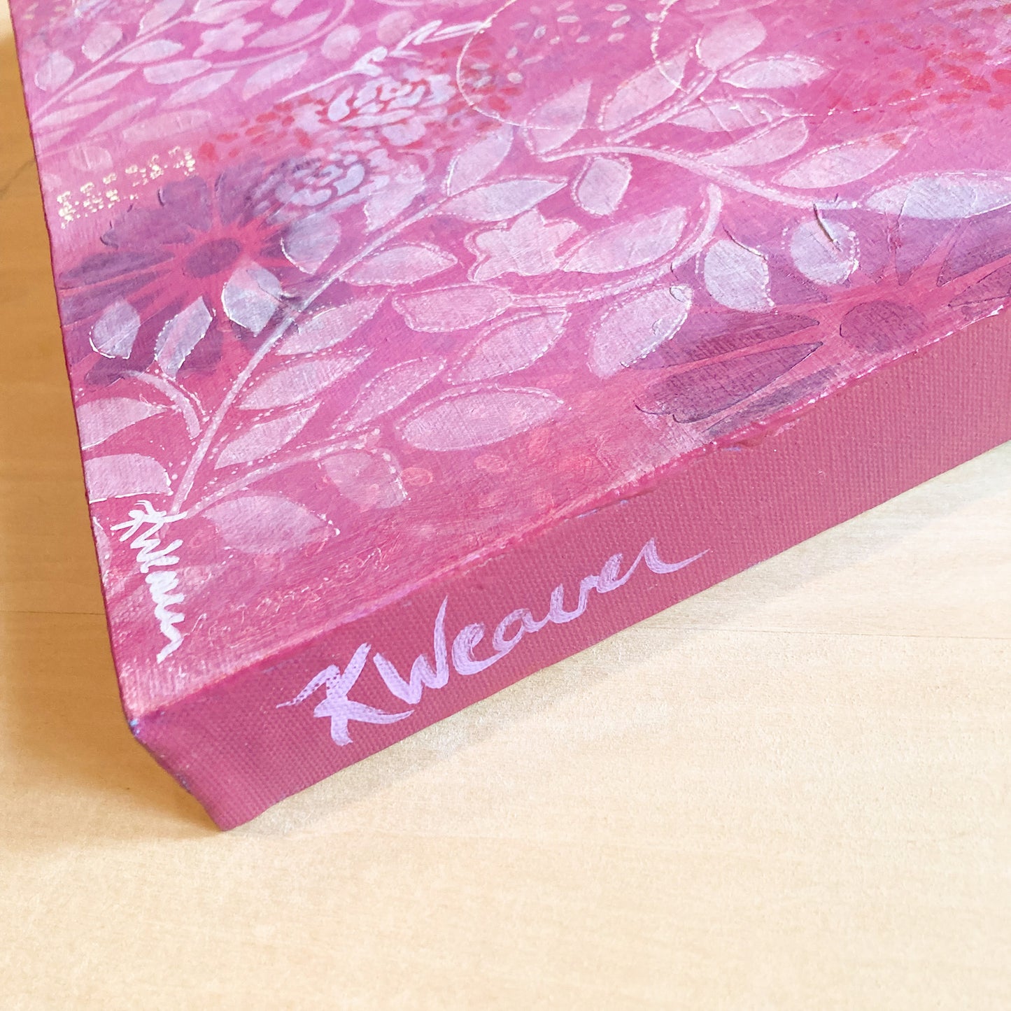 side view of original abstract painting with warm pink background white roses and leaf prints dark flowers layered underneath emits warm feeling of love